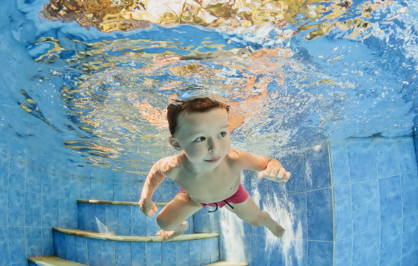 Маленький мальчик плавает под водой в бассейне