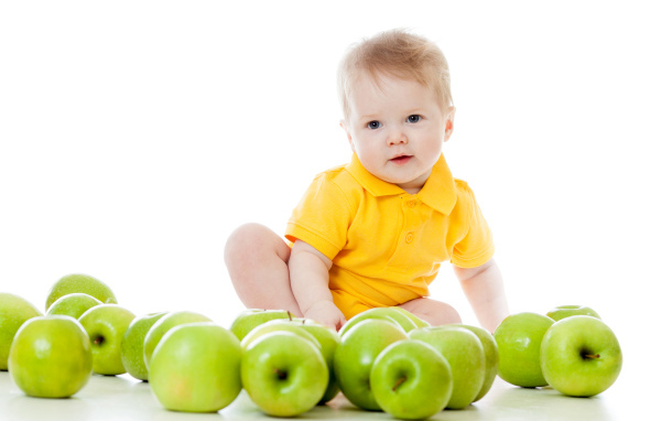 Маленький мальчик с зелеными яблоками на белом фоне
