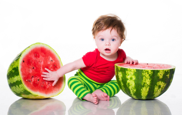 Маленький мальчик с половинами арбуза на белом фоне