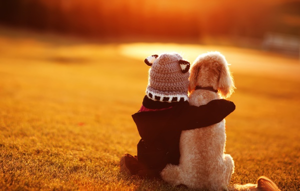 Маленький ребенок сидит с собакой на траве