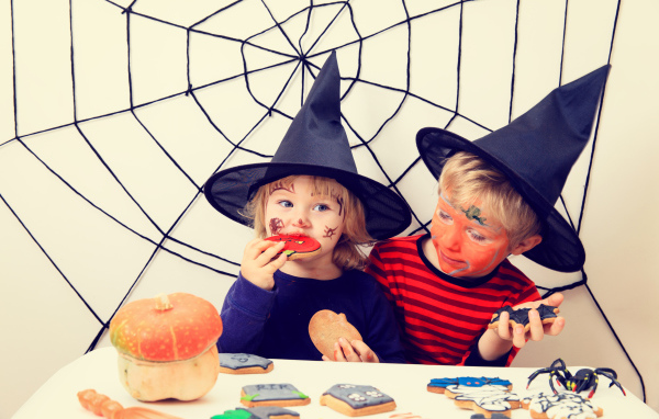 Маленькие дети в костюмах на Хэллоуин едят праздничные сладости