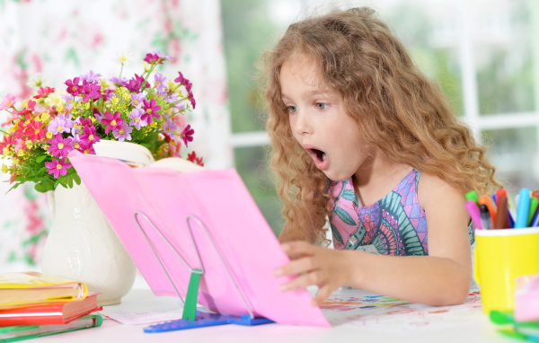 Маленькая русоволосая девочка удивленно смотрит в книгу