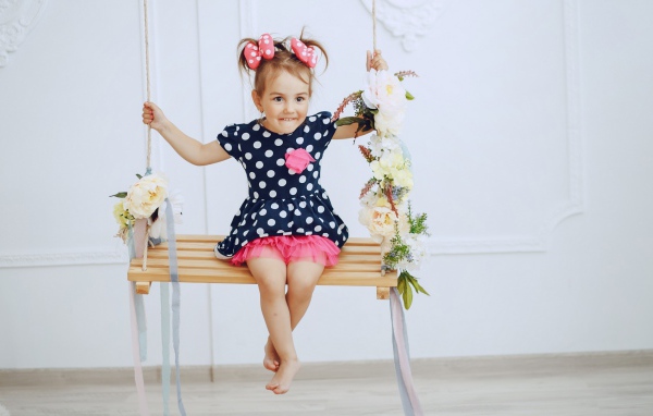 Маленькая забавная девочка в платье в горох  на качели