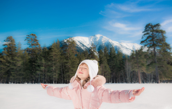 Маленькая девочка в розовой куртке на фоне гор зимой