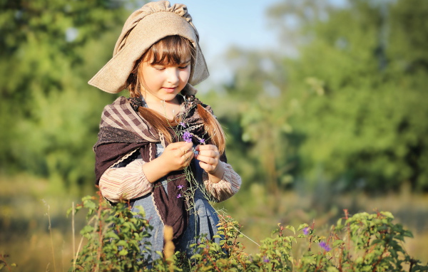 Маленькая девочка в костюме собирает травы