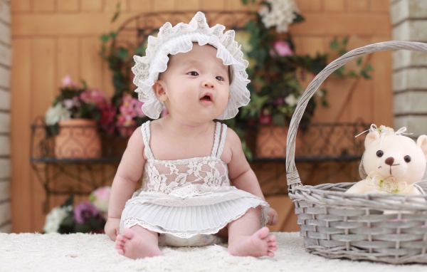 Маленькая девочка в белом платье с медвежонком в корзине