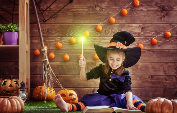 Маленькая девочка в костюме ведьмы с волшебной книгой на Хэллоуин