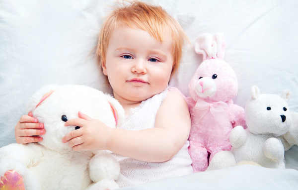 Маленькая девочка лежит в кровати с плюшевыми игрушками