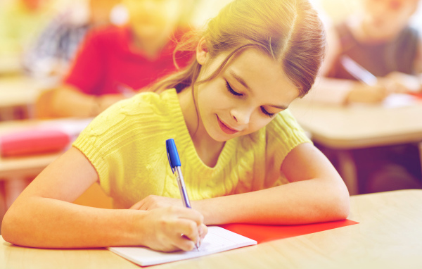 Маленькая девочка школьница пишет ручкой в тетради