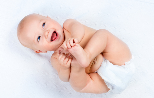 Маленький улыбающийся грудной ребенок держит руками ноги