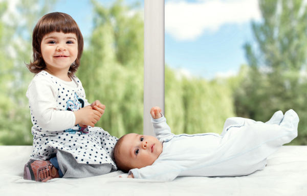 Маленькая улыбающаяся девочка с грудным ребенком