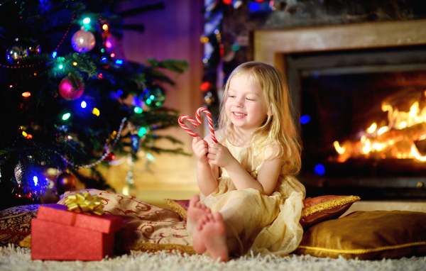 Длинноволосая девочка блондинка с леденцами у новогодней елки