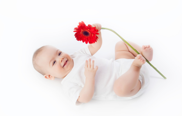 Улыбающийся младенец с цветком красной герберы на белом фоне
