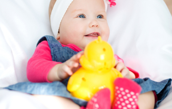 Улыбающаяся голубоглазая девочка младенец с игрушкой в руках