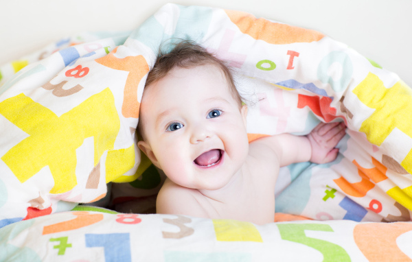 Улыбающийся голубоглазый ребенок под разноцветным покрывалом