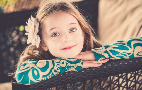 Улыбающаяся зеленоглазая девочка с белым цветком в волосах