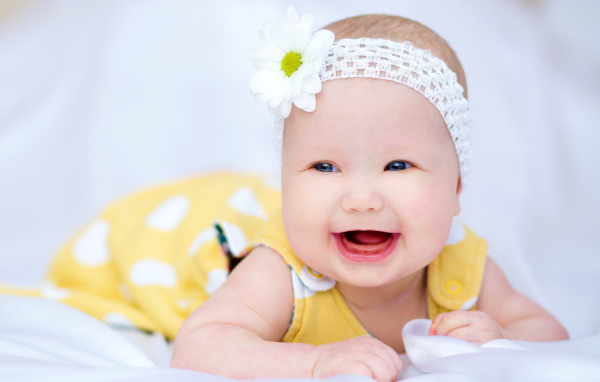 Улыбающаяся маленькая девочка в повязке с белым цветком на голове