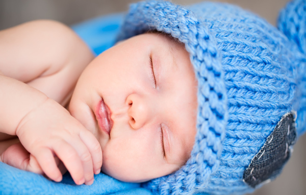 Милый спящий младенец с синей вязаной шапке