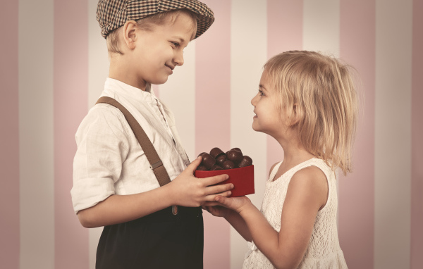 Мальчик дарит девочке коробку шоколадных конфет