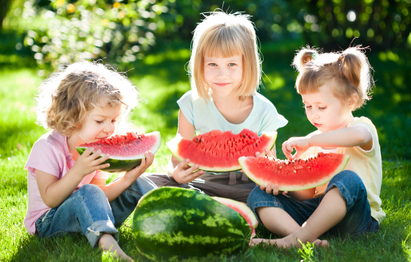 Три маленькие девочки едят арбуз на зеленой траве летом