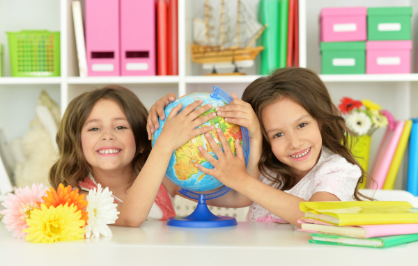 Две маленькие девочки школьницы с глобусом  в руках