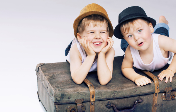 Два маленьких улыбающихся мальчика лежат на старом чемодане