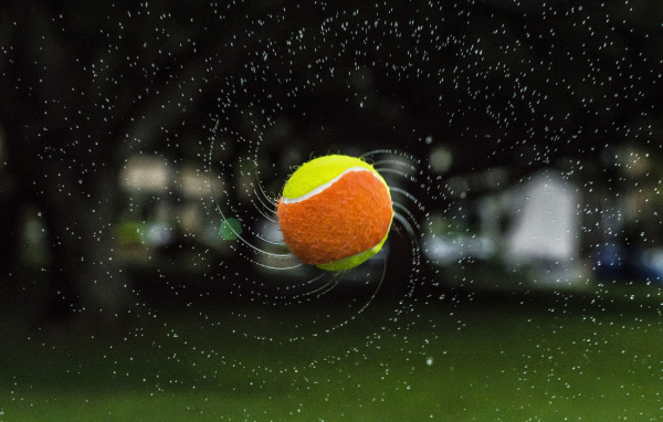 Теннисный мяч летит в каплях воды 