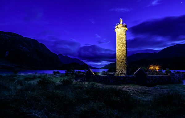 Night lighthouse off the coast in the background of the mountains, the village of Glenfinnan. Scotland