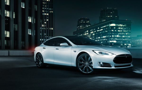 Белый электромобиль Тесла на фоне города 