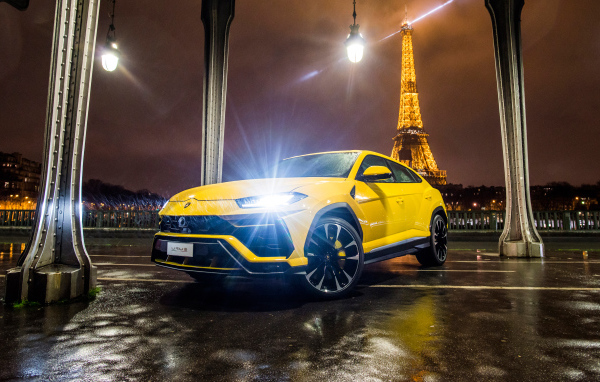 Желтый Lamborghini Urus, 2018 с включенными фарами на фоне Эйфелевой башни