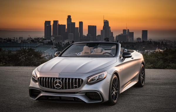Серебристый автомобиль Mercedes AMG S63 4MATIC Cabriolet, 2018 на фоне мегаполиса