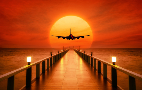 The airplane is landing at sunset over the ocean