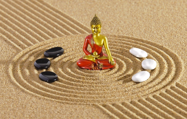 Статуэтка Будды стоит на песке с рисунком и камнями