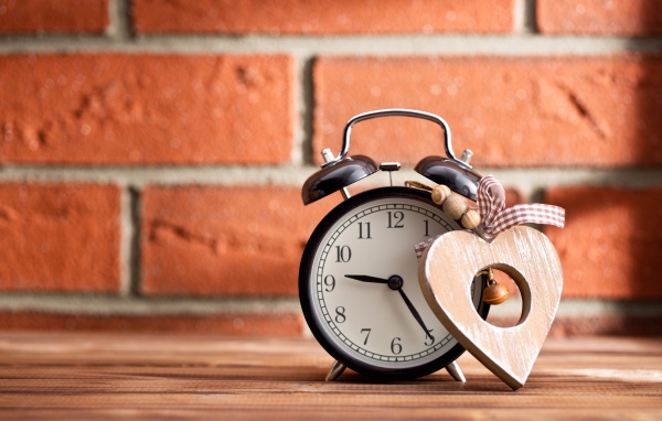 Будильник с деревянным сердцем стоит на фоне стены