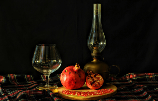 Керосиновая лампа, гранат и бокал на черном фоне
