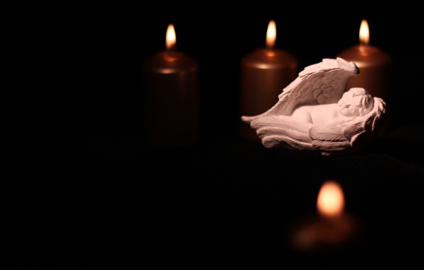 Фигурка ангела освещен горящими свечами на черном фоне