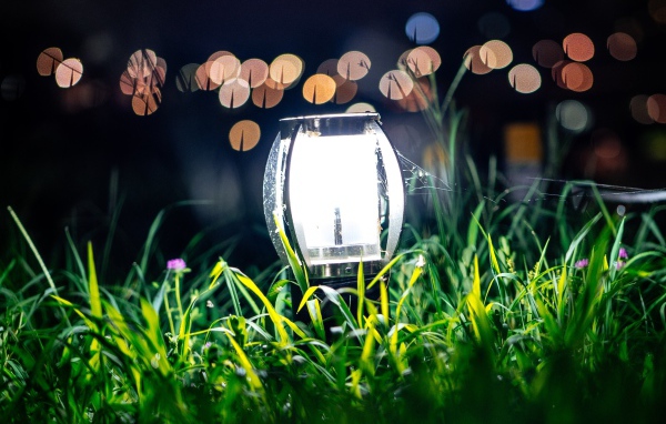 Включенный фонарь стоит в зеленой траве