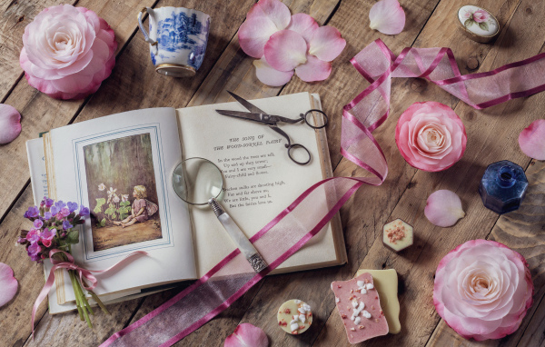 Старая книга на столе с увеличительным стеклом и искусственными цветами