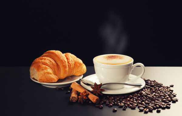 Чашка кофе на столе кофейными зернами, бадьяном, корицей  круассаном 