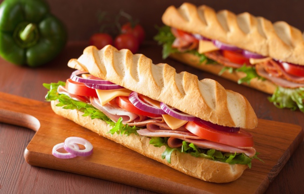 Аппетитный сэндвич с ветчиной, листьями салата, помидорами и луком