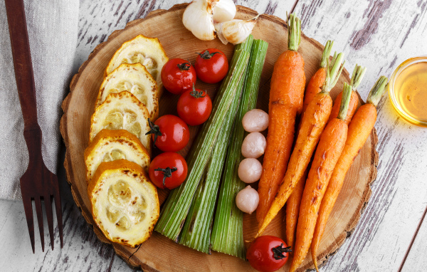 Печеные кабачки, помидоры, морковь, сельдерей и чеснок на разделочной доске