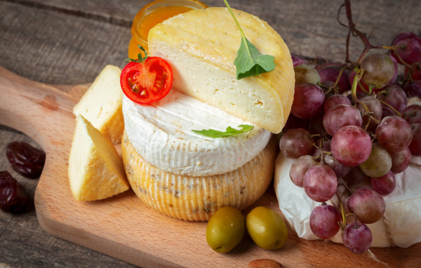 Сыр на разделочной доске с виноградом и оливками