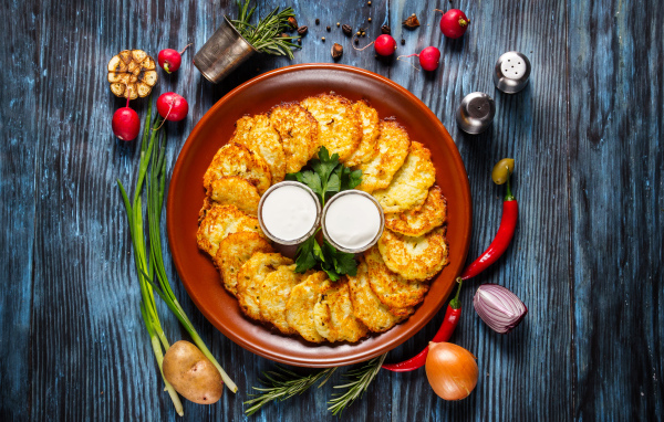 Драники с соусом на тарелке на столе с овощами