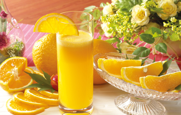 Свежий апельсиновый сок на столе с фруктами и цветами