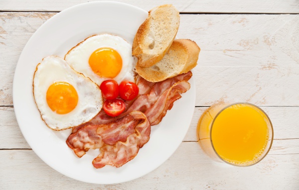 Яичница с беконом, гренками и помидорами на столе с соком 
