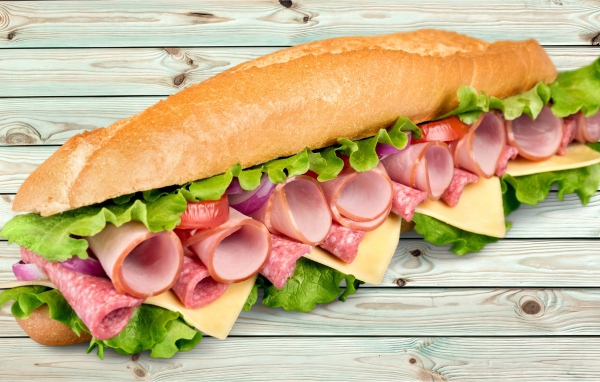 Большой бутерброд с колбасой, сыром и листьями салата