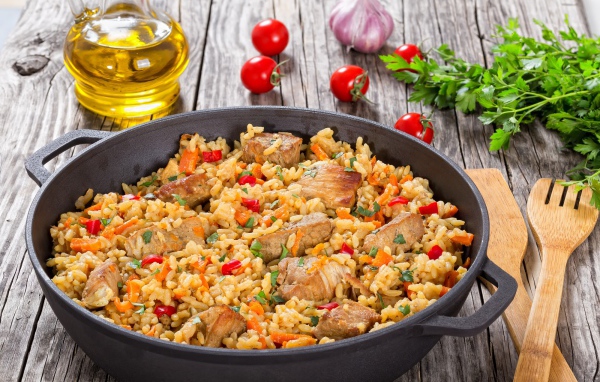 Плов с мясом на столе с помидорами и зеленью петрушки