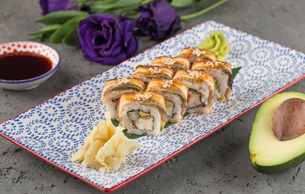 Роллы с авокадо и соевым соусом на столе с цветами 