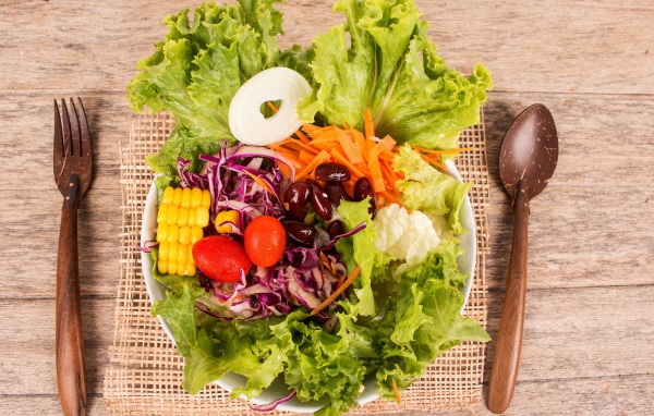 Салат с овощами и зелеными листьями салата в тарелке на столе со столовыми приборами