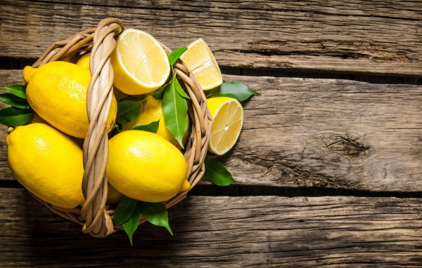 Красивые желтые лимоны в корзине на деревянном столе